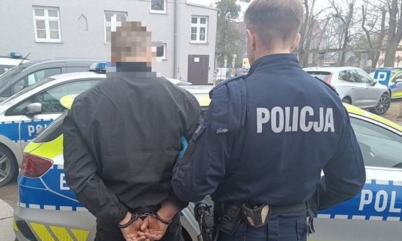 Policjant z zatrzymanym mężczyzna zakutym w kajdanki.