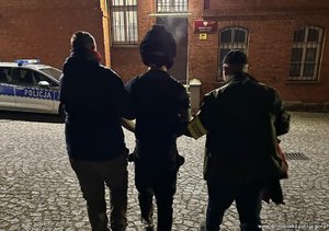 Dwóch policjantów prowadzi zatrzymanego mężczyznę.