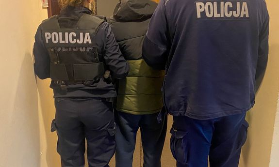 Dwoje umundurowanych policjantów z zatrzymanym mężczyzną. Widok z tyłu.