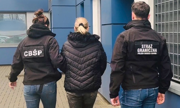 Dwoje funkcjonariuszy prowadzi zatrzymaną osobę.