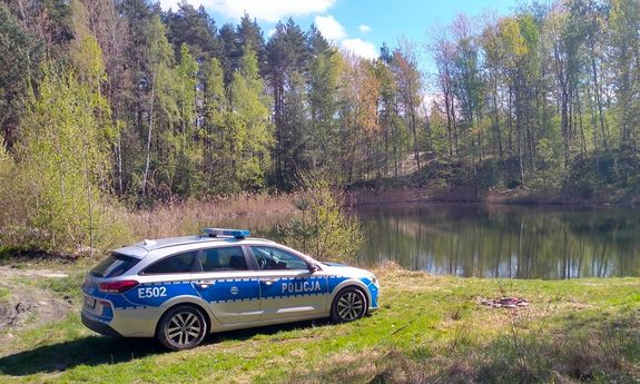 Policyjny radiowóz zaparkowany przy zbiorniku wodnym w lesie.