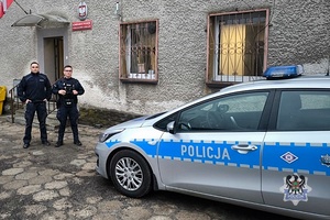 Policjanci w mundurach stoją obok radiowozu.