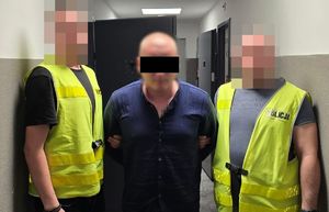 Dwaj policjanci z zatrzymanym mężczyzną zakutym w kajdanki.