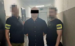 Dwaj policjanci z zatrzymanym mężczyzną zakutym w kajdanki.