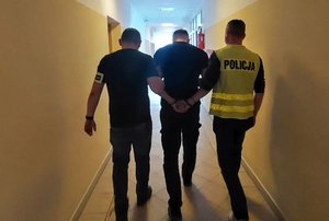 dwóch policjantów idzie z zatrzymanym.