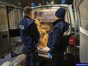Dwaj policjanci przy radiowozie, w którym siedzi okryty kocem ratunkowym senior.