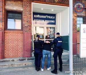 Policjant i policjantka wprowadzają do budynku komisariatu zatrzymanego mężczyznę.