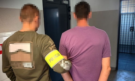 Policjant trzyma zatrzymanego mężczyznę zakutego w kajdanki.