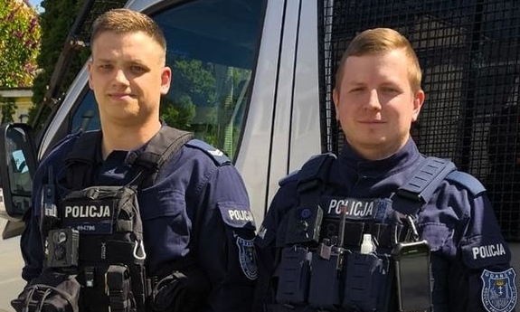 Dwaj policjanci, którzy uratowali życie mężczyźnie na lotnisku stoją przy radiowozie.
