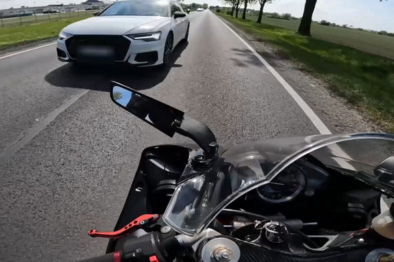 Stop klatka na którym widać kierującego audi wyprzedzającego na trzeciego. Nagranie z kamerki zainstalowanej na kasku kierującego motocyklem.
