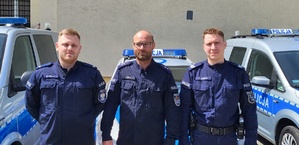 Na zdjęciu trzech umundurowanych policjantów. Za nimi trzy radiowozy.