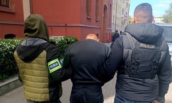 Dwaj funkcjonariusze prowadzą zatrzymanego męczyznę.