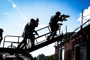 Kontrterroryści wchodzą po platformie na dach budynku.