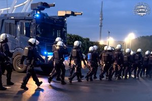 Maszerujący policjanci w umundurowaniu i w kaskach.