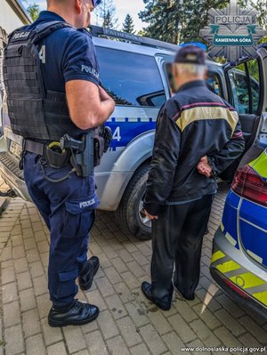 policjant stoi przy radiowozie, obok stoi uratowany mężczyzna.