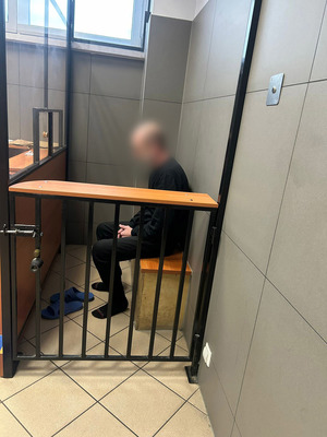 Zatrzymany siedzi w pomieszczeniu dla zatrzymanych, zakuty w kajdanki.