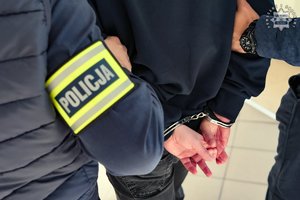 Zatrzymany mężczyzna w kajdankach prowadzony przez funkcjonariuszy.