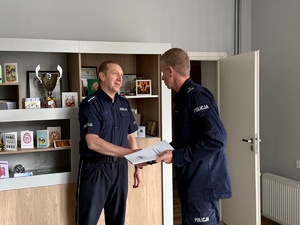 Umundurowany policjant ściska dłoń drugiemu policjantowi.