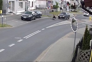 Stopklatka z nagrania monitoringu przedstawia miejsce kolizji opisane w tekście. Samochód na przejściu dla pieszych i osoba potrącona siedząca na drodze przy samochodzie.