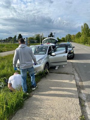 Funkcjonariusz z zatrzymanym siedzącym na skraju drogi, za nimi w głębi przy drodze pojazdy.