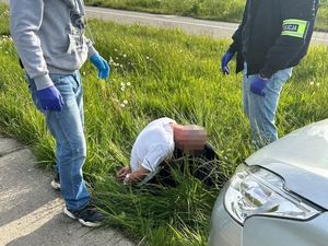 Zatrzymany siedzi w trawie, obok niego stoją dwaj funkcjonariusze.