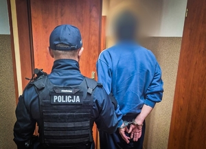 Umundurowany policjant prowadzi zatrzymanego mężczyznę.