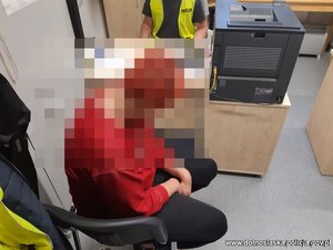 Zatrzymana kobieta siedzi na krześle w pomieszczeniu.
