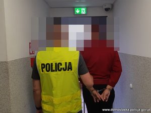 Policjant prowadzi zatrzymaną kobietę.