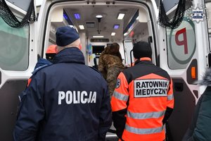 Policjant i ratownik medyczny stoją przy otwartych drzwiach karetki.
