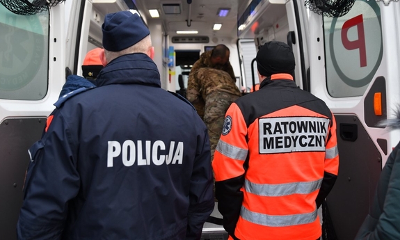 Policjant i ratownik medyczny stoją przy otwartych drzwiach karetki.