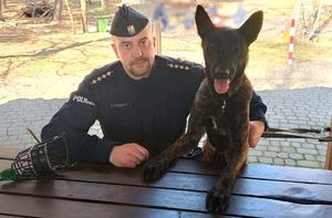 Siedzący przy stole policjant i pies służbowy.