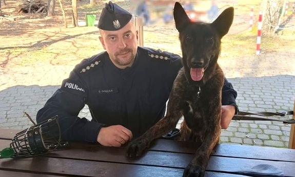 Siedzący przy stole policjant i pies służbowy.