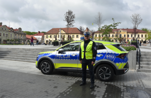 policjant stoi przed radiowozem.