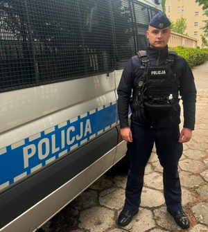 policjant stoi obok radiowozu.