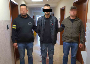 Dwaj funkcjonariusze z zatrzymanym mężczyzna w kajdankach.