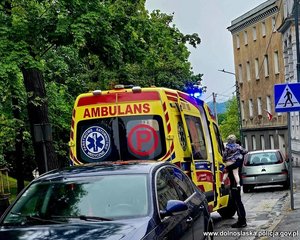 Kobieta trzyma dziecko na rękach stojąc przed drzwiami karetki.