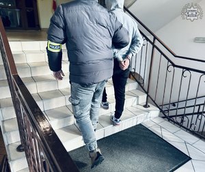 Funkcjonariusz prowadzi po schodach zatrzymanego.