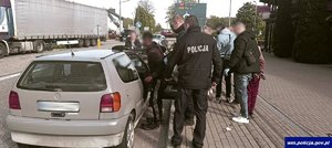 Policjanci i zatrzymane osoby przy samochodzie osobowym.