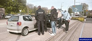 Policjanci i zatrzymane osoby przy samochodzie osobowym.