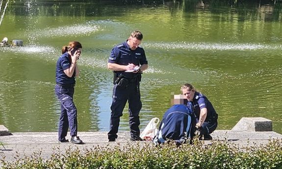 policjanci stoją na brzegu, obok siedzi uratowany mężczyzna.