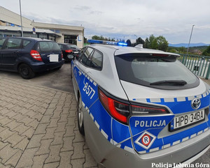 Radiowóz policyjny i inne samochody na parkingu przed szpitalem.