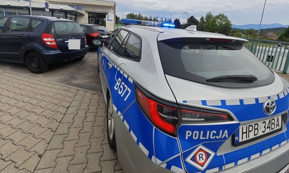 Radiowóz policyjny i inne samochody na parkingu przed szpitalem.
