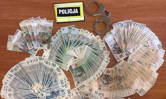 Banknoty leżą na stole, obok kajdanki i opaska z napisem Policja.