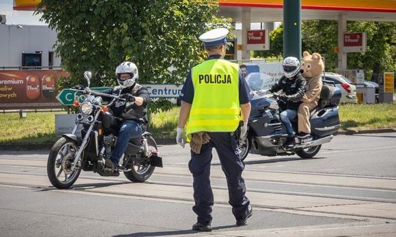 Policjant stoi na drodze, przed nim jeżdżą motocykliści.