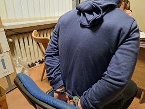 Zatrzymany siedzi na krześle z kajdankami założonymi na ręce trzymane z tyłu.