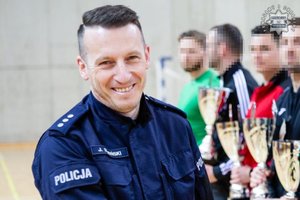 Zastępca Komendanta Komisariatu Policji z Radzionkowa kom. Jarosław Dembiński. W tle zawodnicy trzymający puchary.