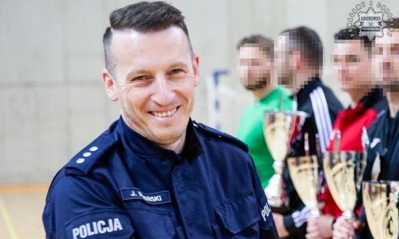 Zastępca Komendanta Komisariatu Policji z Radzionkowa kom. Jarosław Dembiński. W tle zawodnicy trzymający puchary.