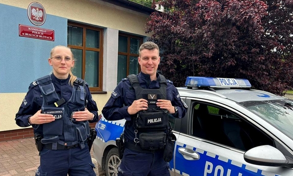 Policjant i policjantka stoją przy radiowozie policyjnym.