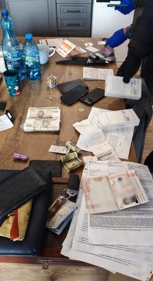 Na stole leżą zabezpieczone przedmioty: dokumenty, pieniądze, telefony komórkowe i inne drobne przedmioty.