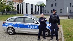Dwoje umundurowanych policjantów przed radiowozem pozuje do zdjęcia.